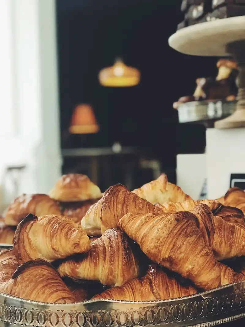 Croissants dourados numa bandeja de aço inox, com o fundo desfocado.